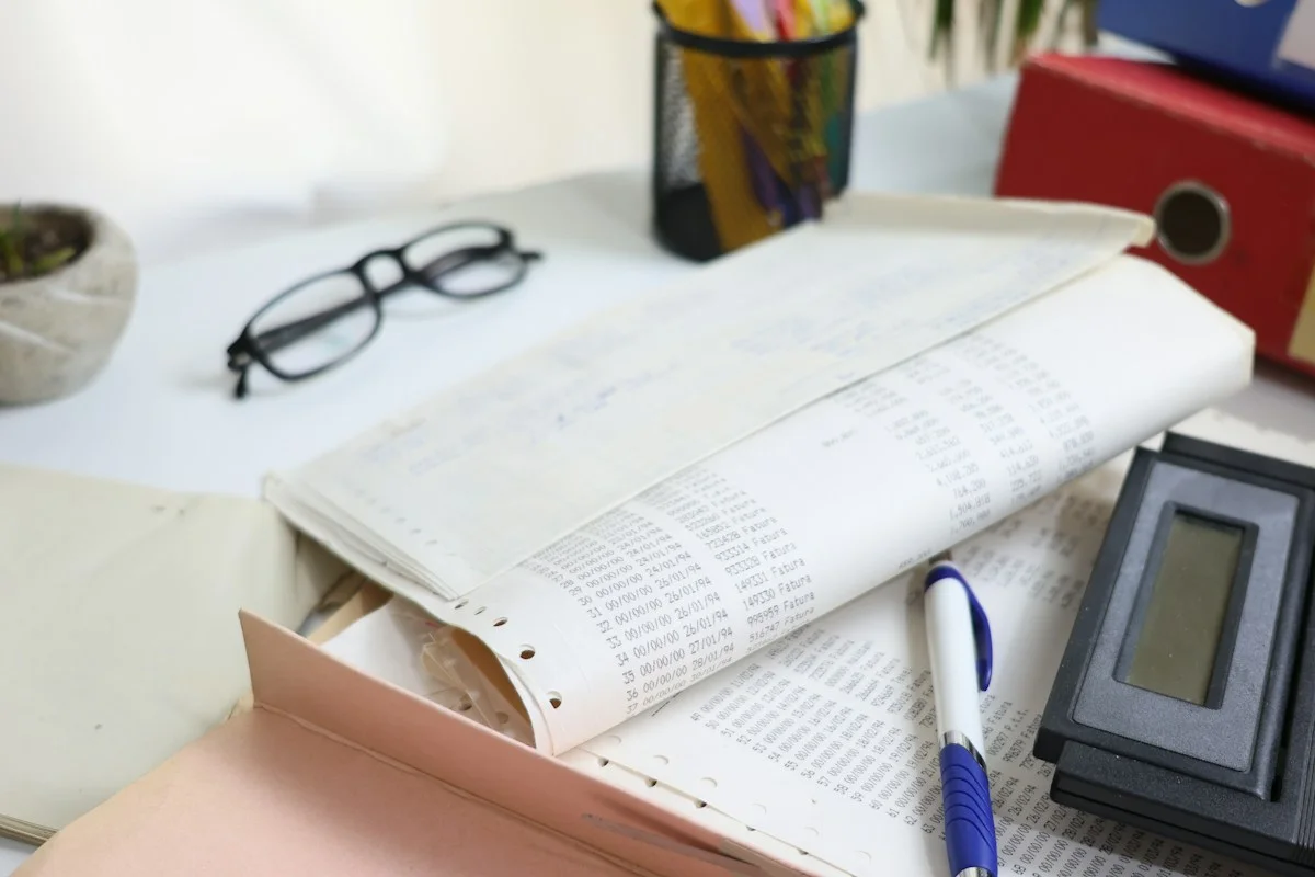 Printed records, glasses, a pen, and a calculator on a desk.